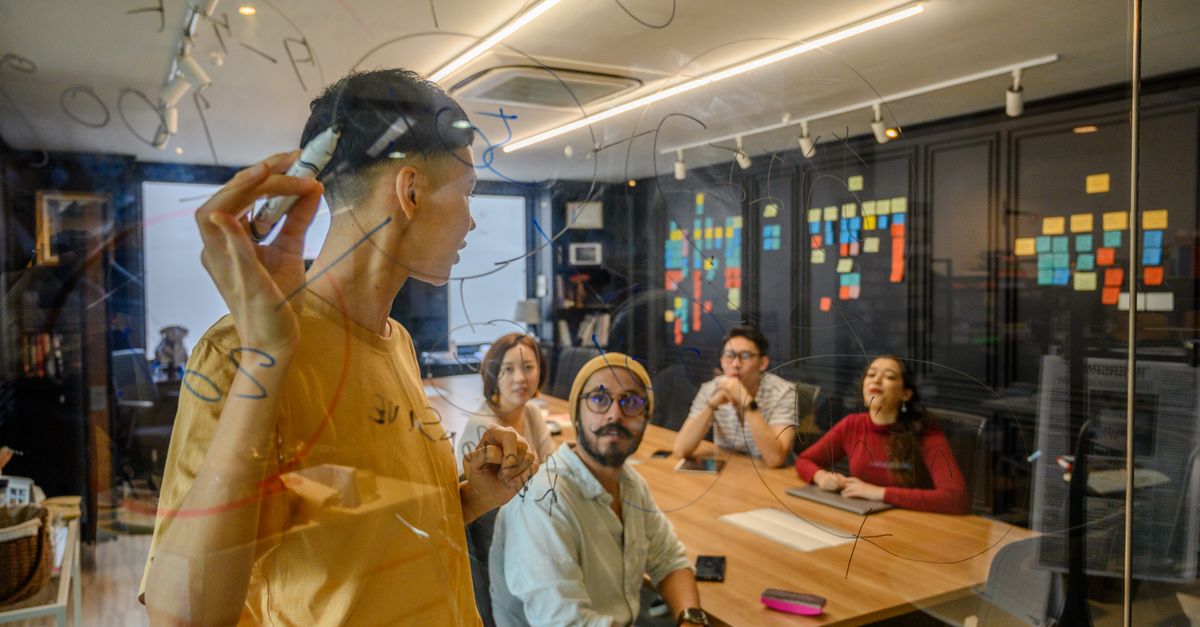 Group of professionals collaborating in an office, brainstorming on glass board.